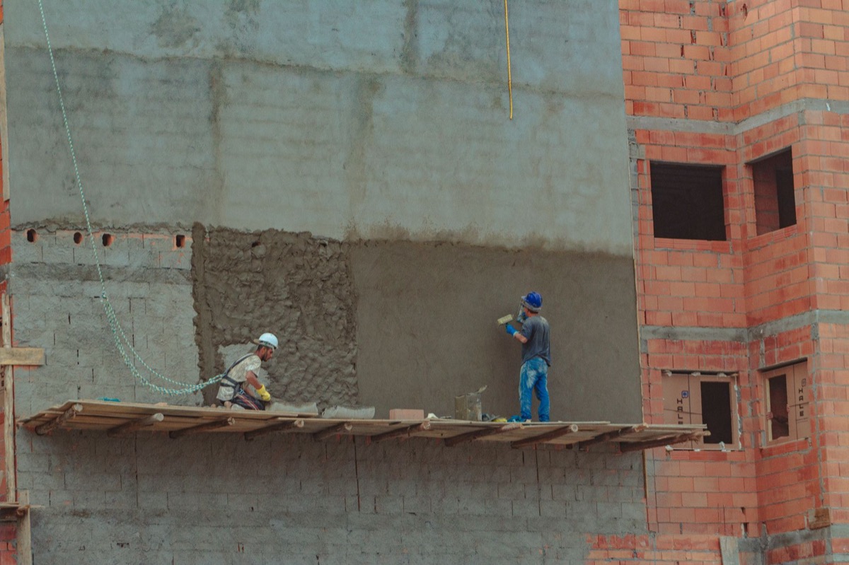 Deux ouvriers appliquant un enduit sur une façade extérieure depuis un échafaudage de chantier